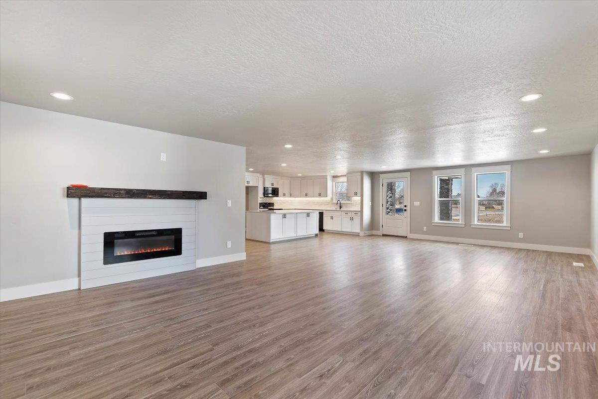 2435 North Black Cat Road Meridian, ID 83646 - Photo 7 of 32 Unfurnished living room with light wood-style flooring, a glass covered fireplace, recessed lighting, and a textured ceiling