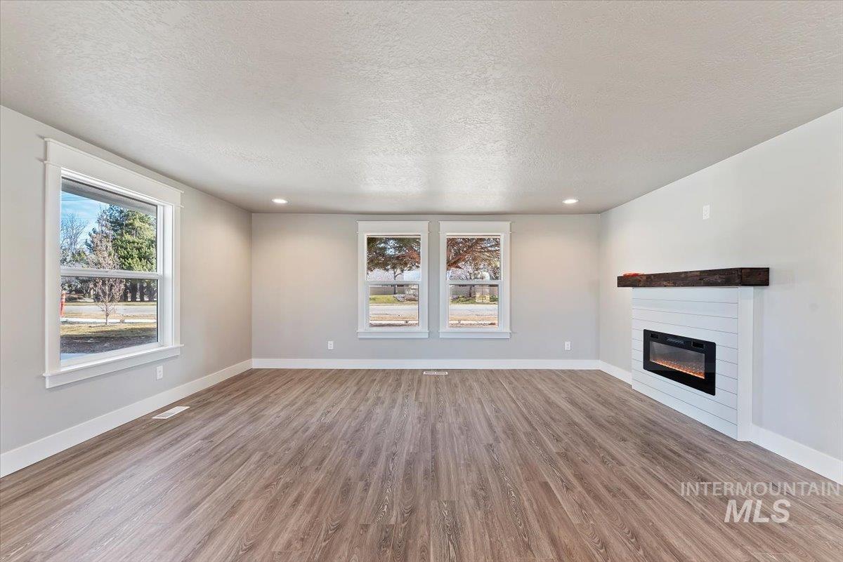 2435 North Black Cat Road Meridian, ID 83646 - Photo 8 of 32 Unfurnished living room with light wood finished floors, a textured ceiling, a glass covered fireplace, and recessed lighting