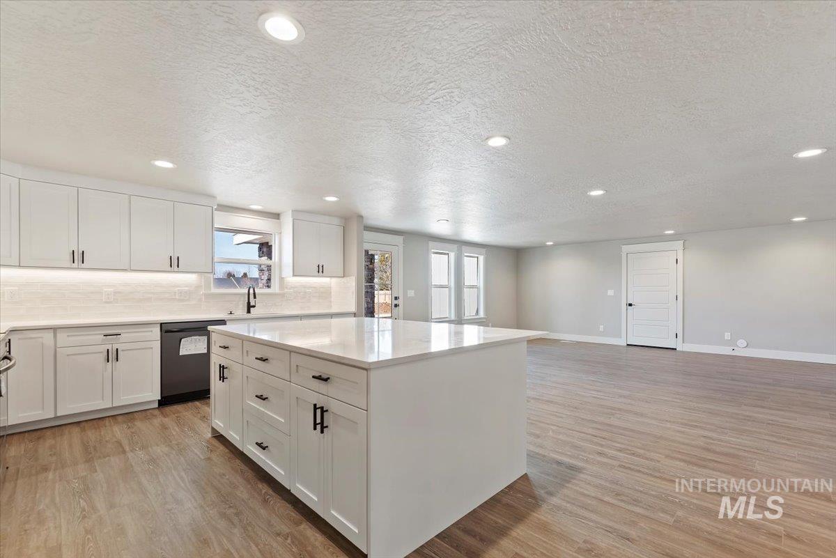 2435 North Black Cat Road Meridian, ID 83646 - Photo 9 of 32 Kitchen featuring a center island, a textured ceiling, backsplash, white cabinets, and light wood finished floors
