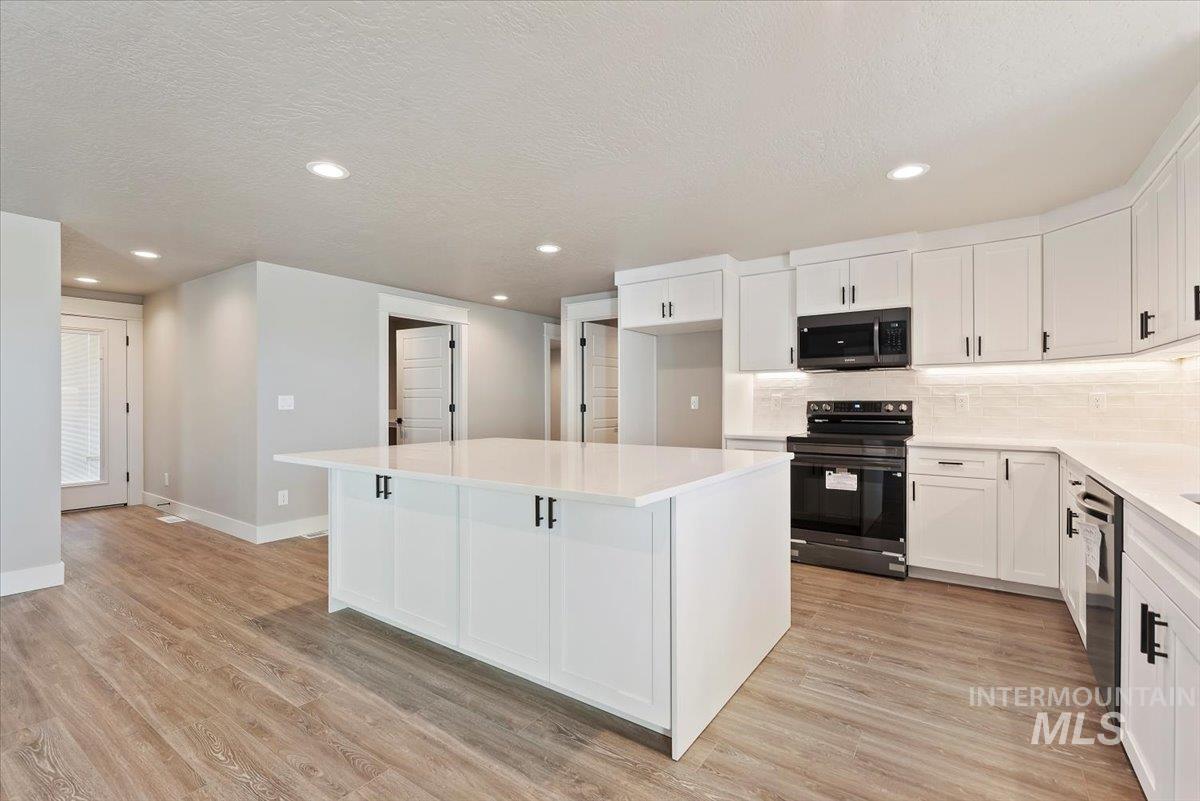 2435 North Black Cat Road Meridian, ID 83646 - Photo 10 of 32 Kitchen featuring white cabinets, stainless steel appliances, a center island, backsplash, and light wood-style flooring