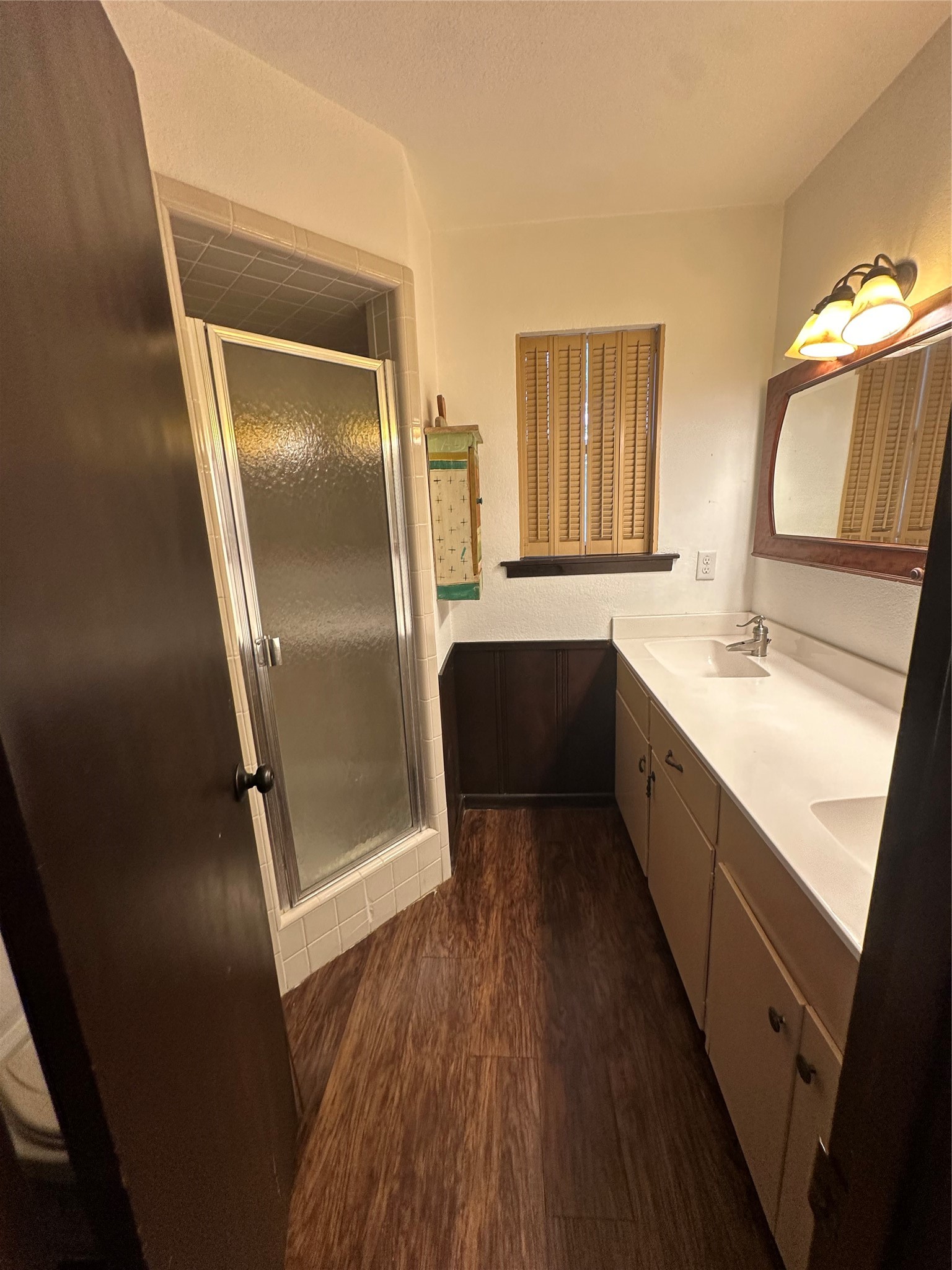 1604 Hailey Street, Unit B Conroe, TX 77301 - Photo 8 of 9 An overall view from the bathroom entrance illustrates the relationship between the double vanity, the window, the mirror, and the corner stall shower, emphasizing the room's practical layout and warm atmosphere.
