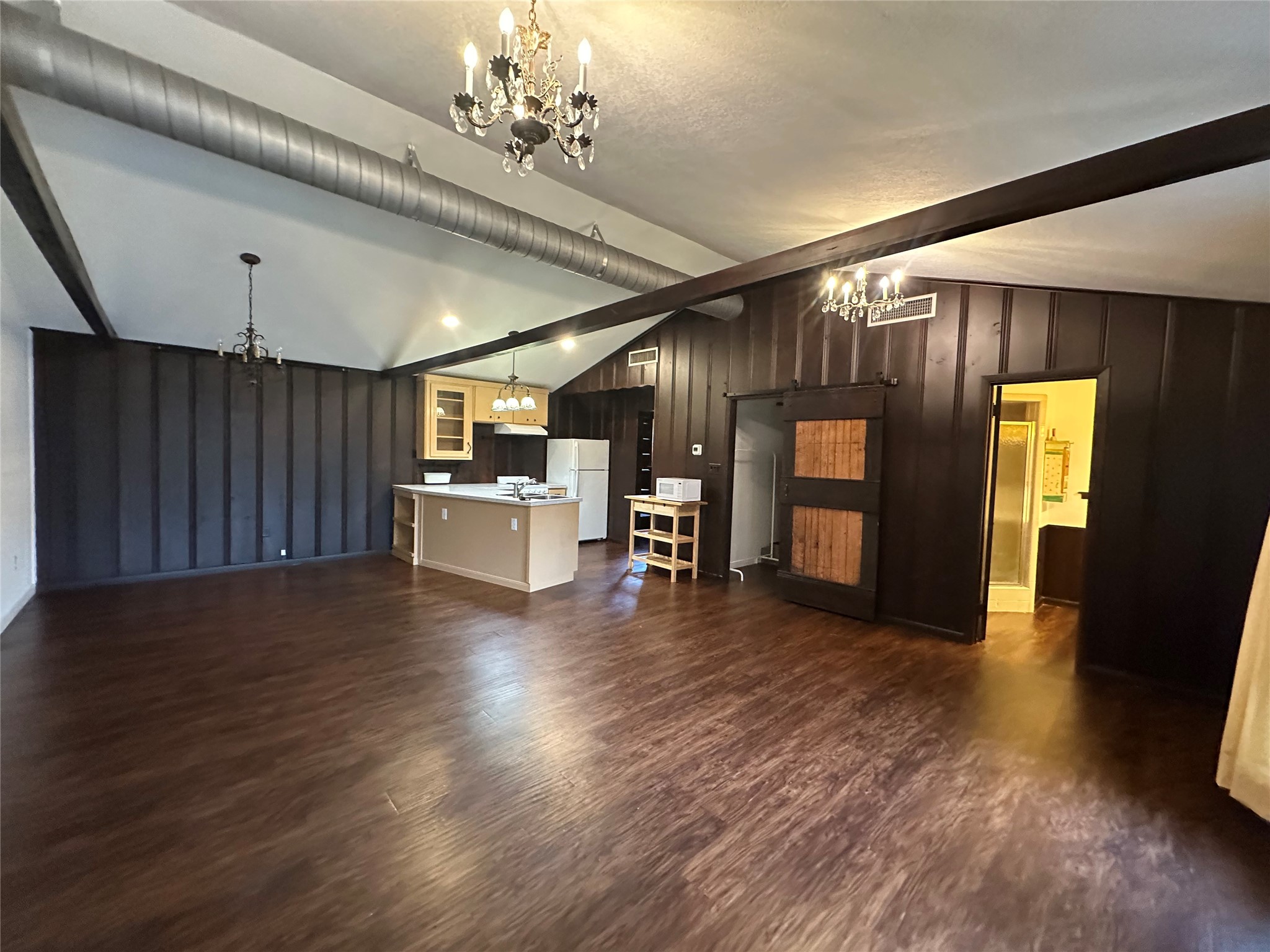 1604 Hailey Street, Unit B Conroe, TX 77301 - Photo 9 of 9 This expansive great room boasts vaulted ceilings with exposed dark wood beams and industrial-style exposed ductwork. Dark wood-paneled walls surround the entire area, creating a rustic feel that flows effortlessly between the living, dining, and open kitchen spaces, anchored by beautiful dark wood like vinyl planks flooring and a classic crystal chandelier.
