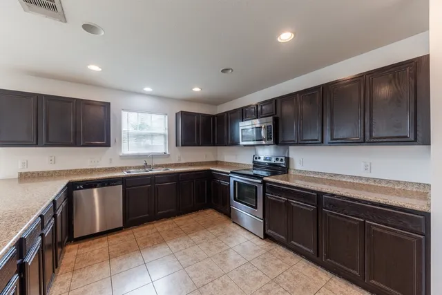 a large kitchen with stainless steel appliances granite countertop wooden cabinets a stove top oven a sink and dishwasher