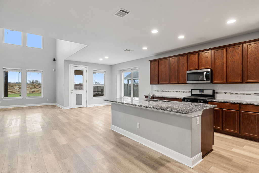 5208 Anaheim Avenue Pflugerville, TX 78660 - Photo 12 of 38 a kitchen with stainless steel appliances granite countertop a stove top oven a sink dishwasher a microwave oven and a refrigerator with wooden floor