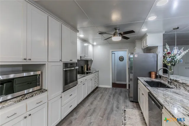 a kitchen with granite countertop a sink stainless steel appliances and white cabinets