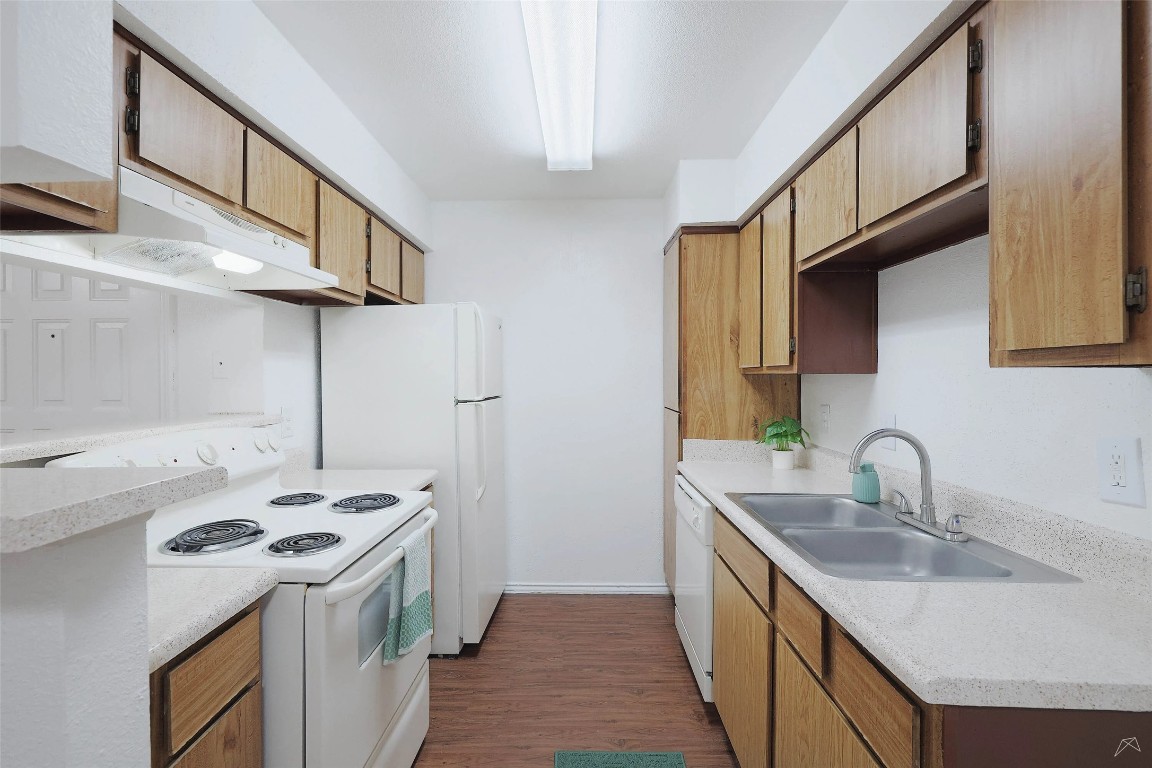 2323 Wells Branch Parkway, Unit C102 Austin, TX 78728 - Photo 16 of 20 Kitchen with white appliances, dark wood-type flooring, under cabinet range hood, and brown cabinets