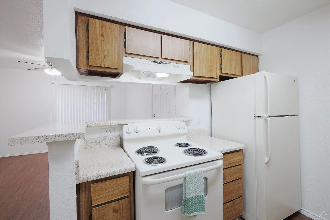 2323 Wells Branch Parkway, Unit C102 Austin, TX 78728 - Photo 7 of 20 Kitchen featuring white appliances, under cabinet range hood, brown cabinetry, and dark wood finished floors