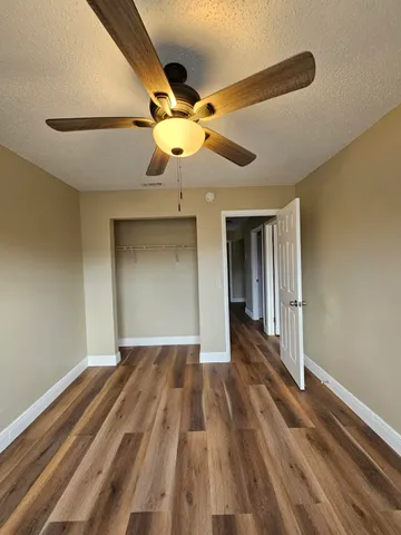 a view of an empty room with wooden floor and a ceiling fan