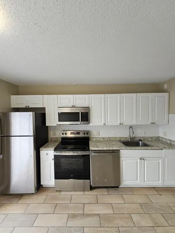 a kitchen with granite countertop a refrigerator sink and white cabinets