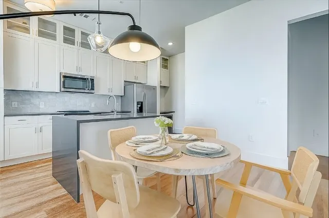 a kitchen with stainless steel appliances granite countertop a sink a stove a dining table and chairs with wooden floor