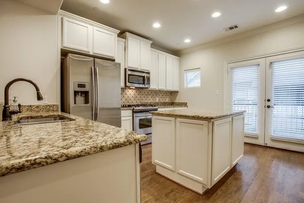 a kitchen with stainless steel appliances granite countertop a refrigerator a stove and a sink with wooden floor
