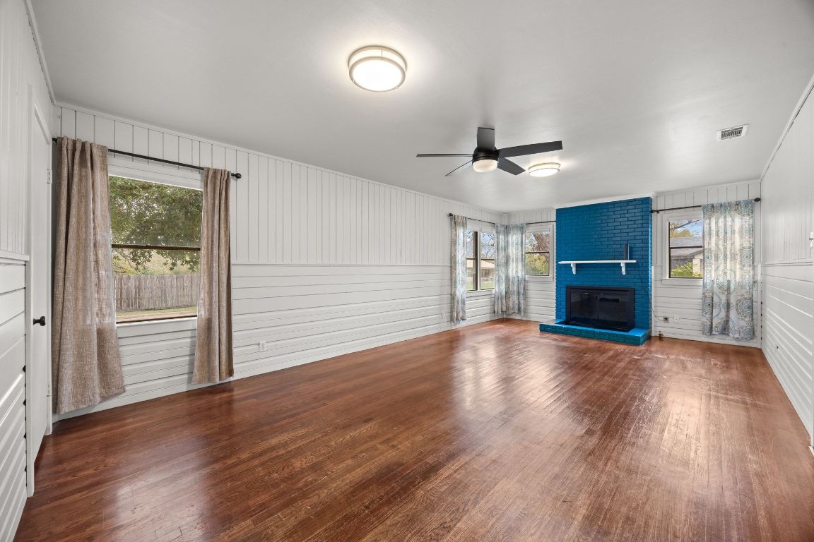 1815 Eckhardt Street Taylor, TX 76574 - Photo 5 of 33 an empty room with wooden floor a ceiling fan a fireplace and windows