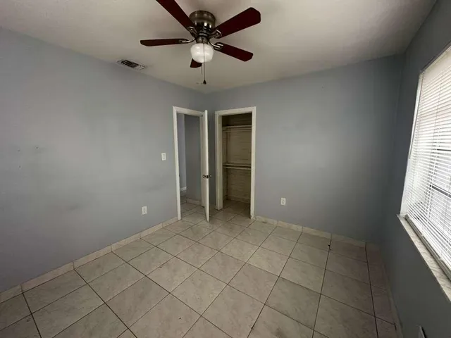an empty room with chandelier fan and windows