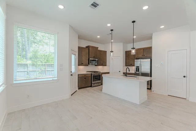 a kitchen with stainless steel appliances kitchen island granite countertop a stove top oven a sink dishwasher a refrigerator and white cabinets with wooden floor