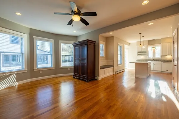 a view of an empty room with wooden floor and a kitchen