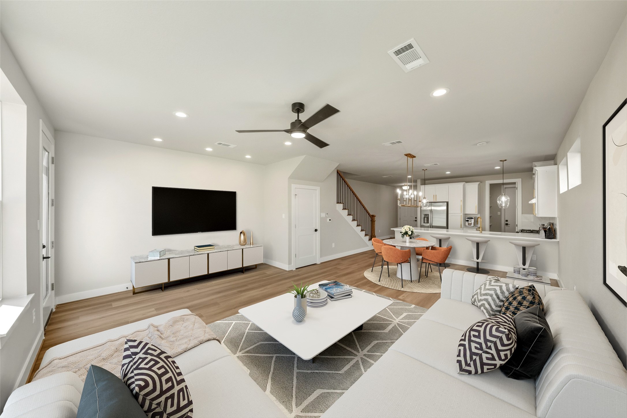 3422 Elser Street Houston, TX 77009 - Photo 4 of 26 This photo showcases a modern open-concept living area with a spacious layout. The room features a comfortable seating area with a large sectional sofa, a wall-mounted TV, and a stylish coffee table. The adjacent dining area has a round table and chic orange chairs. The kitchen includes a breakfast bar with stools, stainless steel appliances, and elegant lighting fixtures. The space is bright and inviting with neutral tones and wood flooring.