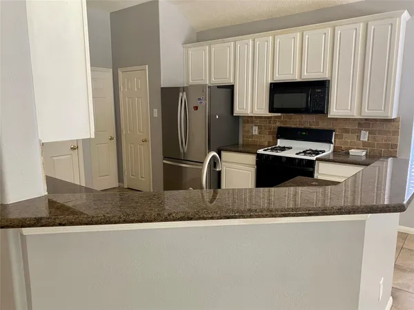 a kitchen with stainless steel appliances granite countertop a sink a stove a microwave a refrigerator a counter space and cabinets