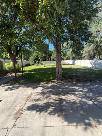 541 300 North Provo, UT 84606 - Photo 6 of 36 Expansive green lawn framed by mature trees, featuring a concrete pad and perimeter fencing