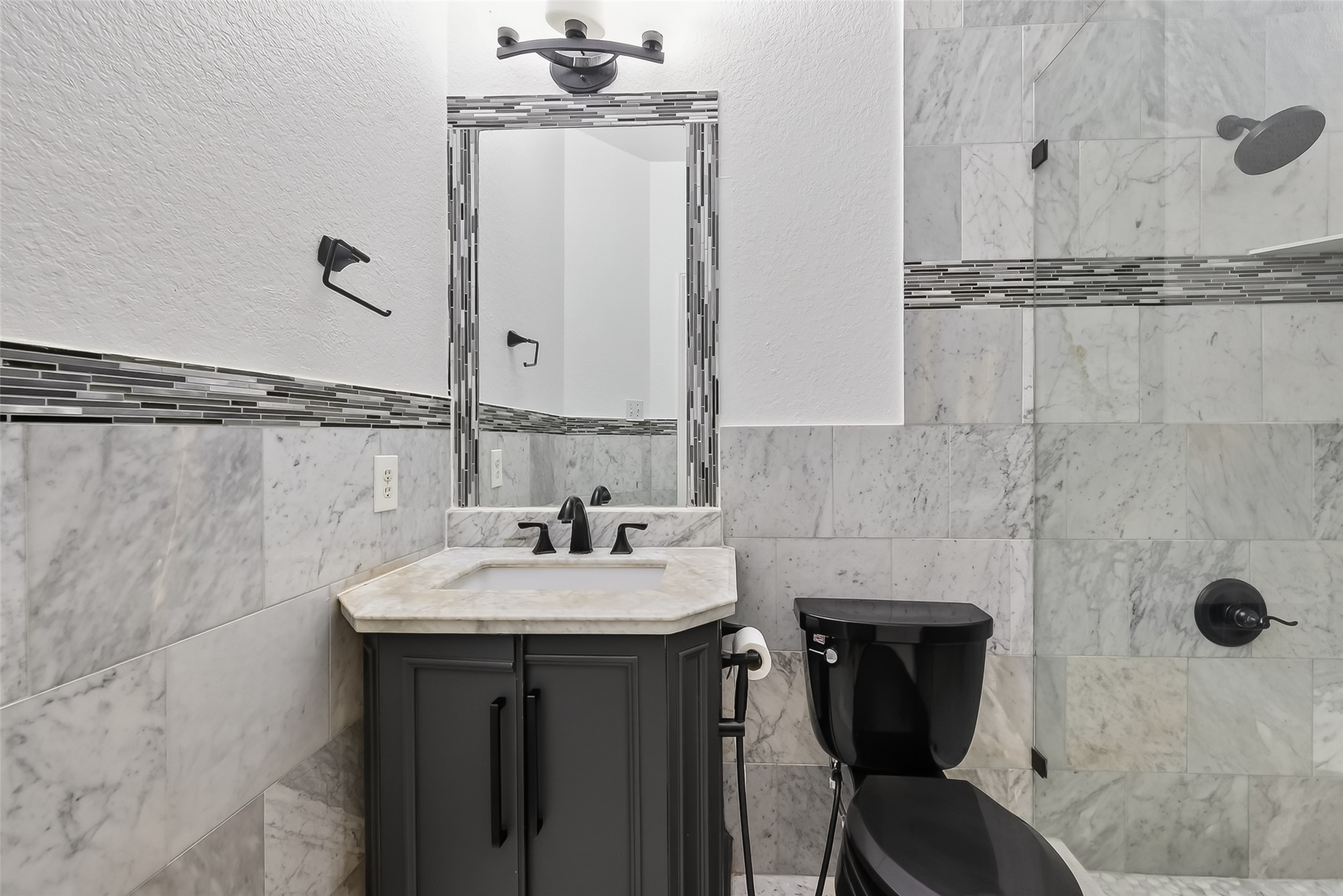 1311 Rene Court Sugar Land, TX 77479 - Photo 28 of 45 This attached bathroom features elegant marble tile, a modern vanity with a sleek black faucet, and a glass-enclosed shower. The design is accented with a decorative tile border, enhancing the contemporary feel.