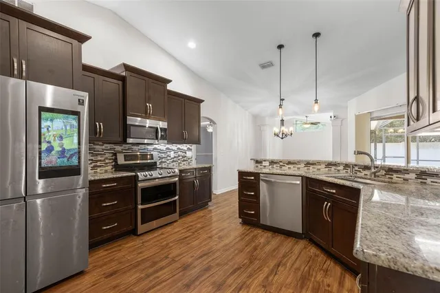 a large kitchen with stainless steel appliances granite countertop a stove a refrigerator and a wooden cabinets