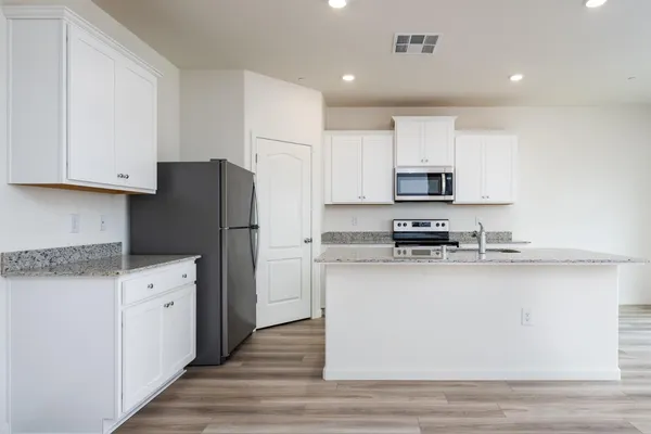 a kitchen with stainless steel appliances granite countertop a refrigerator a stove a sink and white cabinets with wooden floor