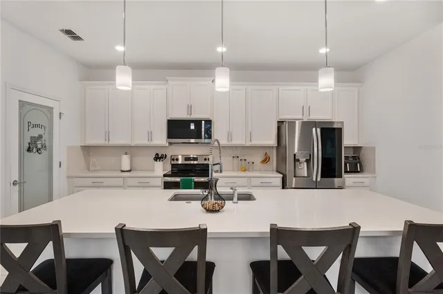 a kitchen with stainless steel appliances kitchen island granite countertop a dining table chairs refrigerator and microwave