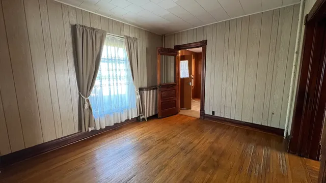 an empty room with wooden floor and windows with curtains