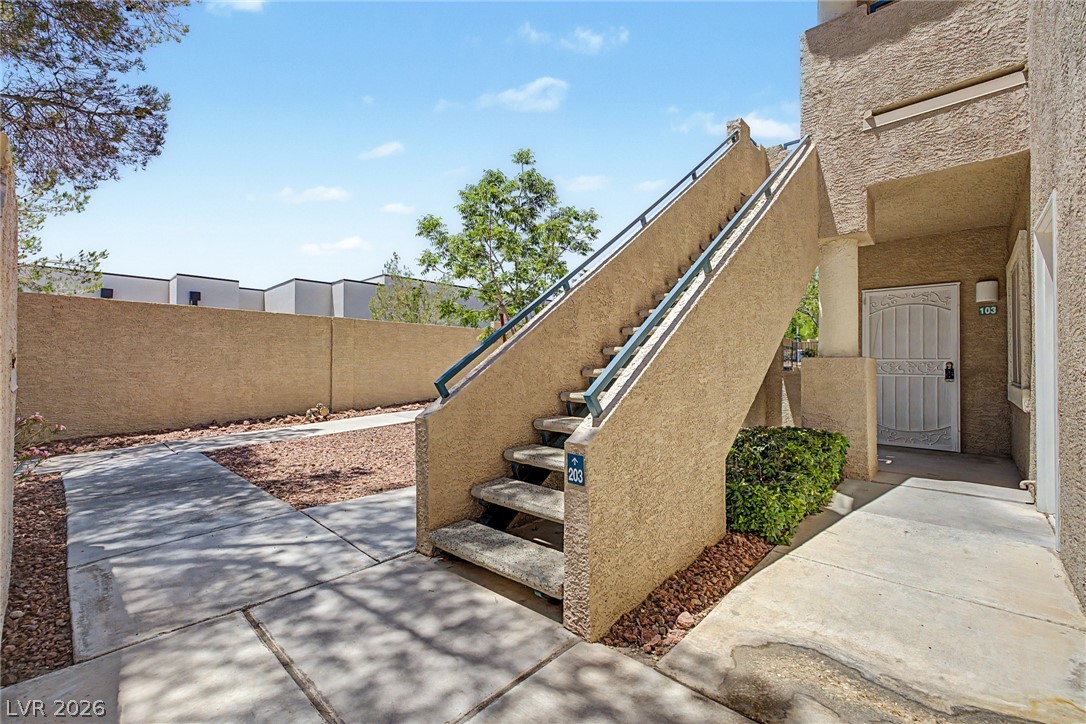 2153 Quarry Ridge Street, Unit 103 Las Vegas, NV 89117 - Photo 9 of 42 Concrete pathways lead to the entrance of a textured stucco building with an outdoor staircase.