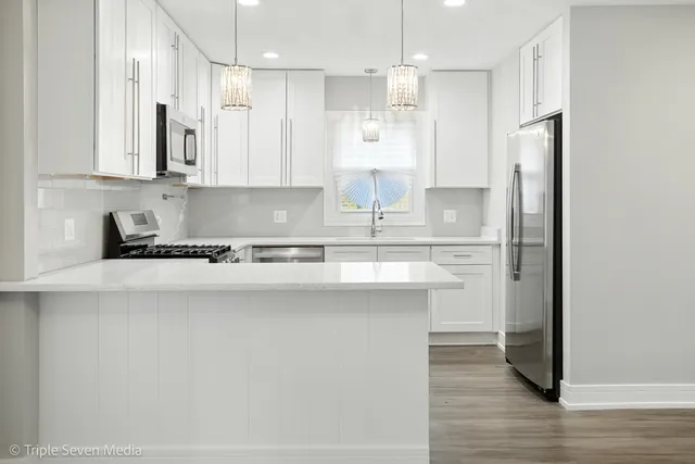 a kitchen with stainless steel appliances granite countertop a sink a refrigerator a white stove and white cabinets with wooden floor