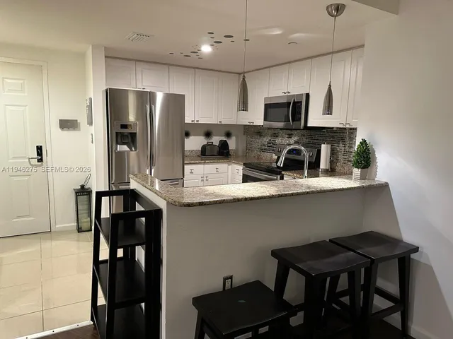 a kitchen with stainless steel appliances granite countertop a refrigerator a stove a sink dishwasher and a microwave with wooden floor