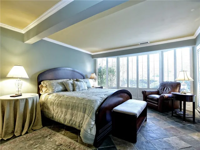 a bedroom with a bed a table chair and a large window