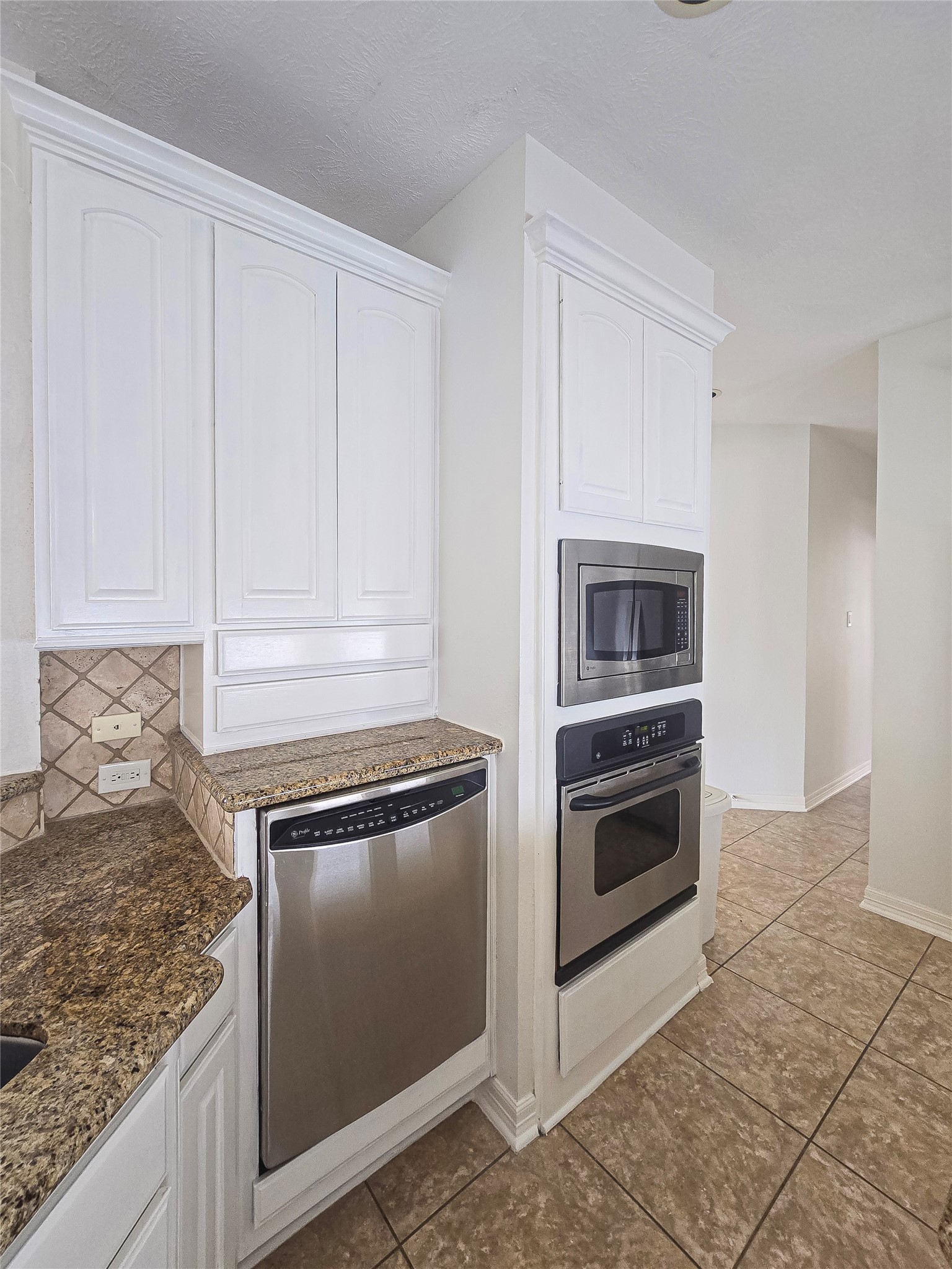 6506 Monte Bello Ridge Lane Houston, TX 77041 - Photo 16 of 39 This kitchen features sleek stainless steel appliances, including a built-in microwave and oven. It has elegant granite countertops, ample white cabinetry, and a tiled floor, offering a modern and functional space.