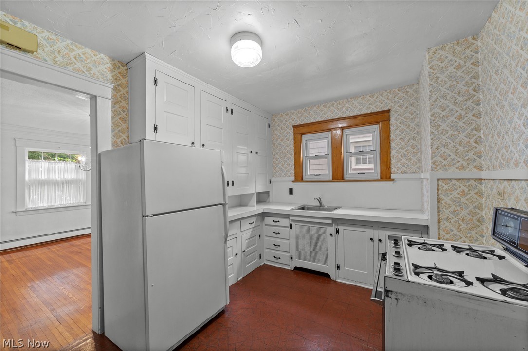 Kitchen with white fridge, dark hardwood / wood-style floors, a baseboard heating unit, white cabinetry, and sink