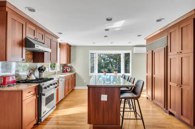 a kitchen with stainless steel appliances granite countertop a stove top oven a sink dishwasher a dining table and chairs with wooden floor