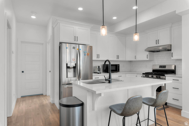 8307 Durham Street Sandy, UT 84070 - Photo 6 of 29 Modern kitchen featuring white cabinetry, light-toned wood-finish flooring, and a central island with a built-in sink and seating space