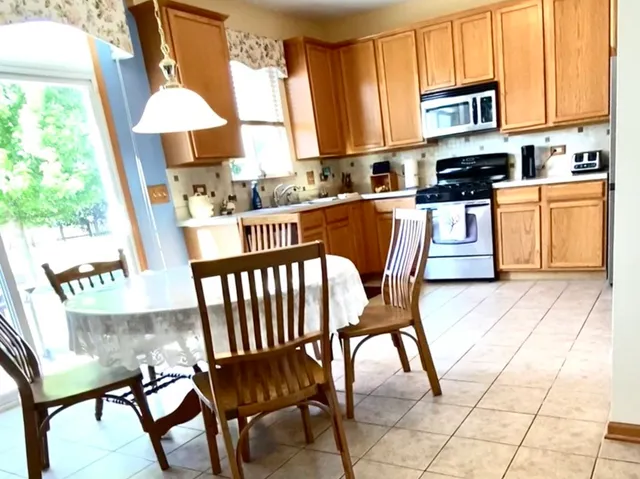 a kitchen with stainless steel appliances kitchen island granite countertop a table chairs and a refrigerator