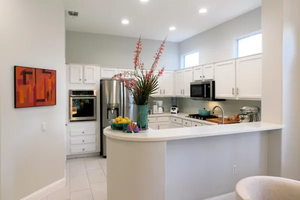 a kitchen with stainless steel appliances a sink a stove a refrigerator a microwave oven with white cabinets and wooden floor