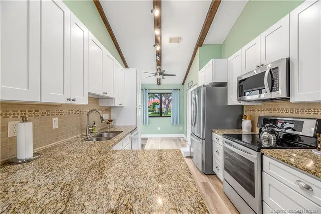 a kitchen with stainless steel appliances granite countertop a refrigerator a sink dishwasher a stove and white countertops with wooden floor