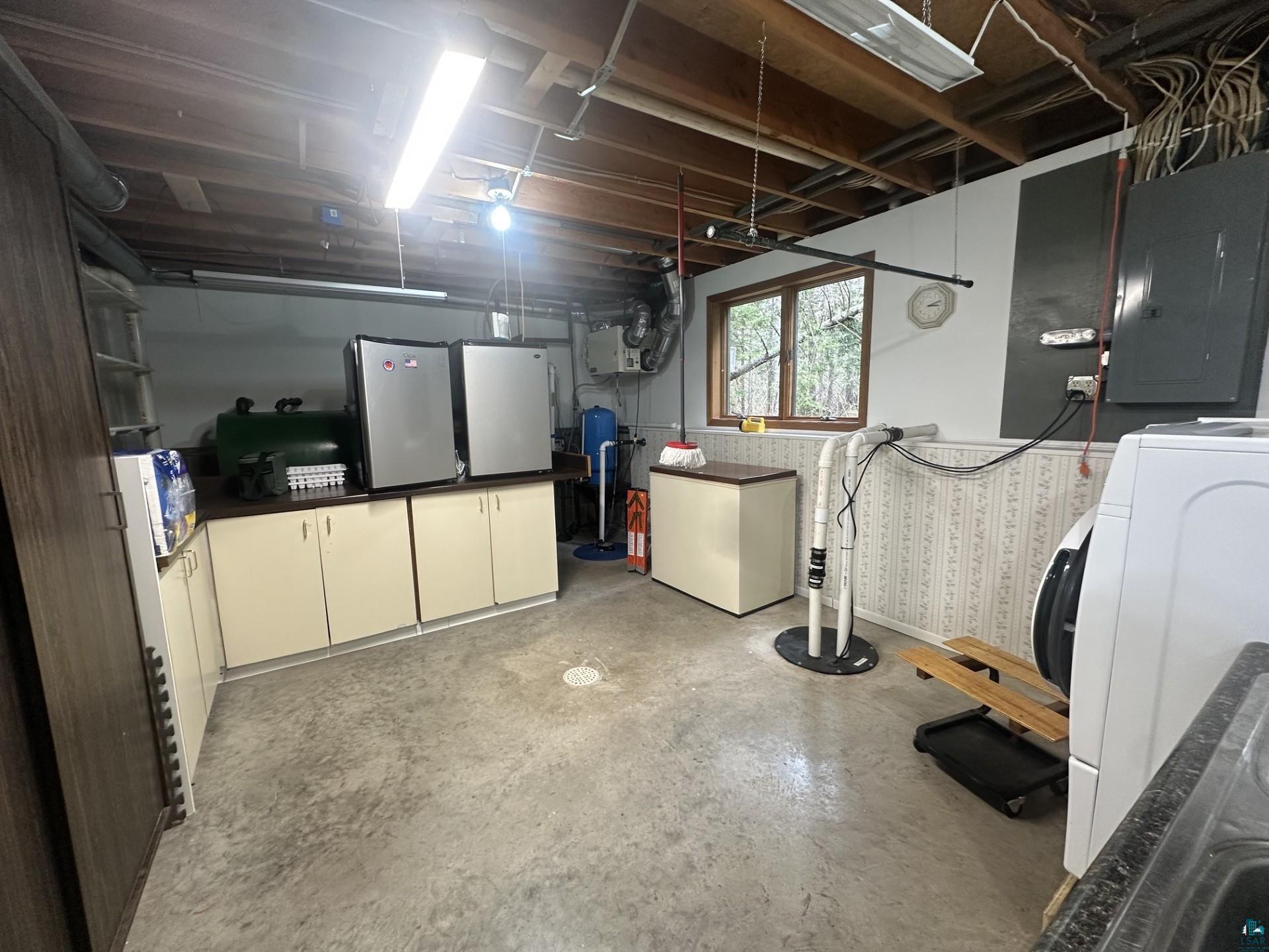 81 Hautaluoma Road Esko, MN 55733 - Photo 26 of 43 Utility room featuring a concrete floor, built-in cabinetry with a dark countertop, a window with natural light, exposed ceiling joists, and a laundry appliance