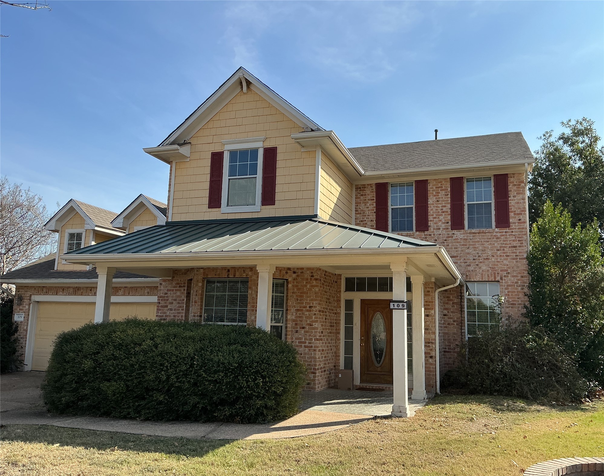 View of front of home featuring brick siding, a porch, driveway, and an attached garage