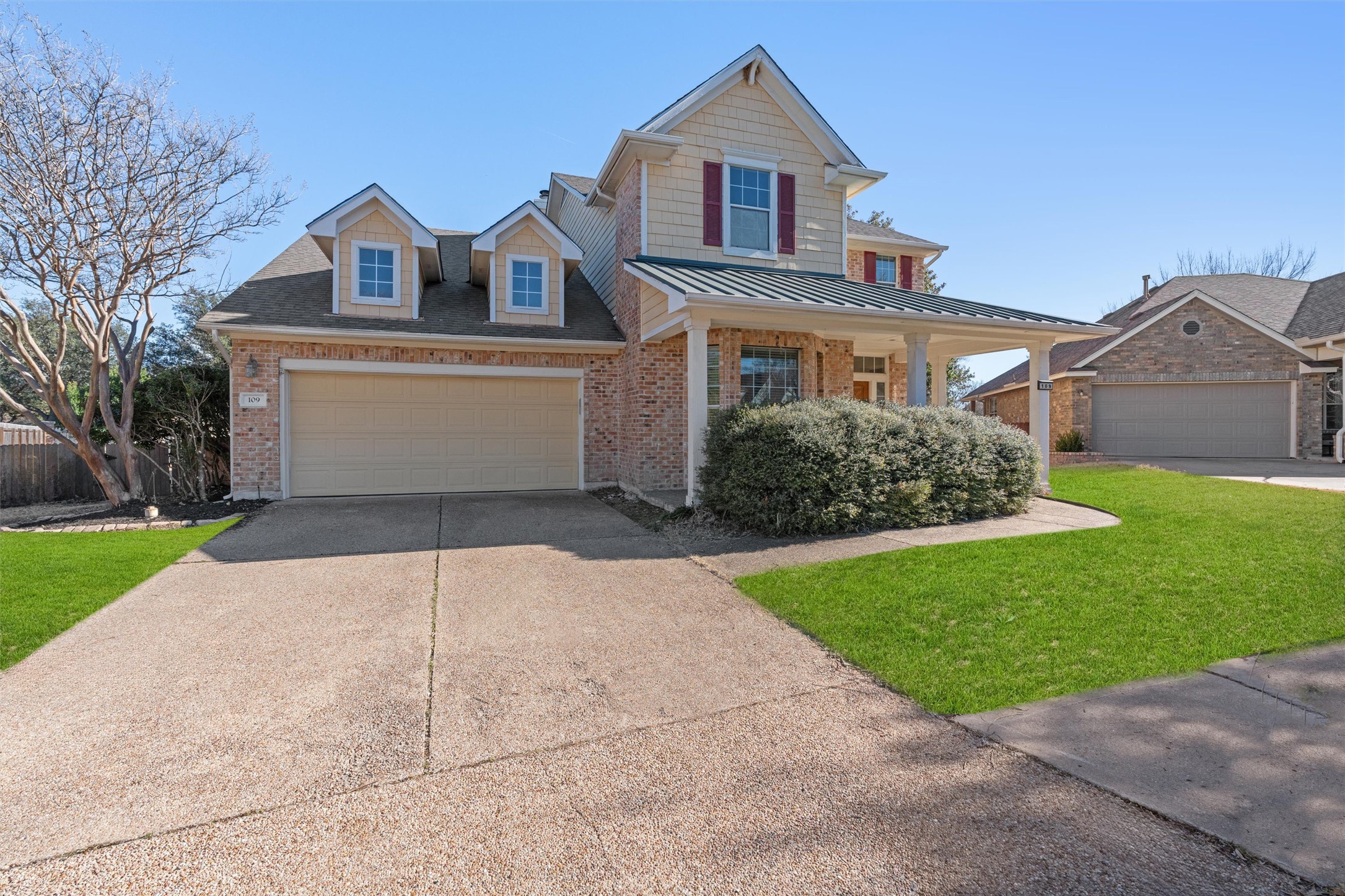 View of front of home with concrete driveway, brick siding, covered porch, and a standing seam roof