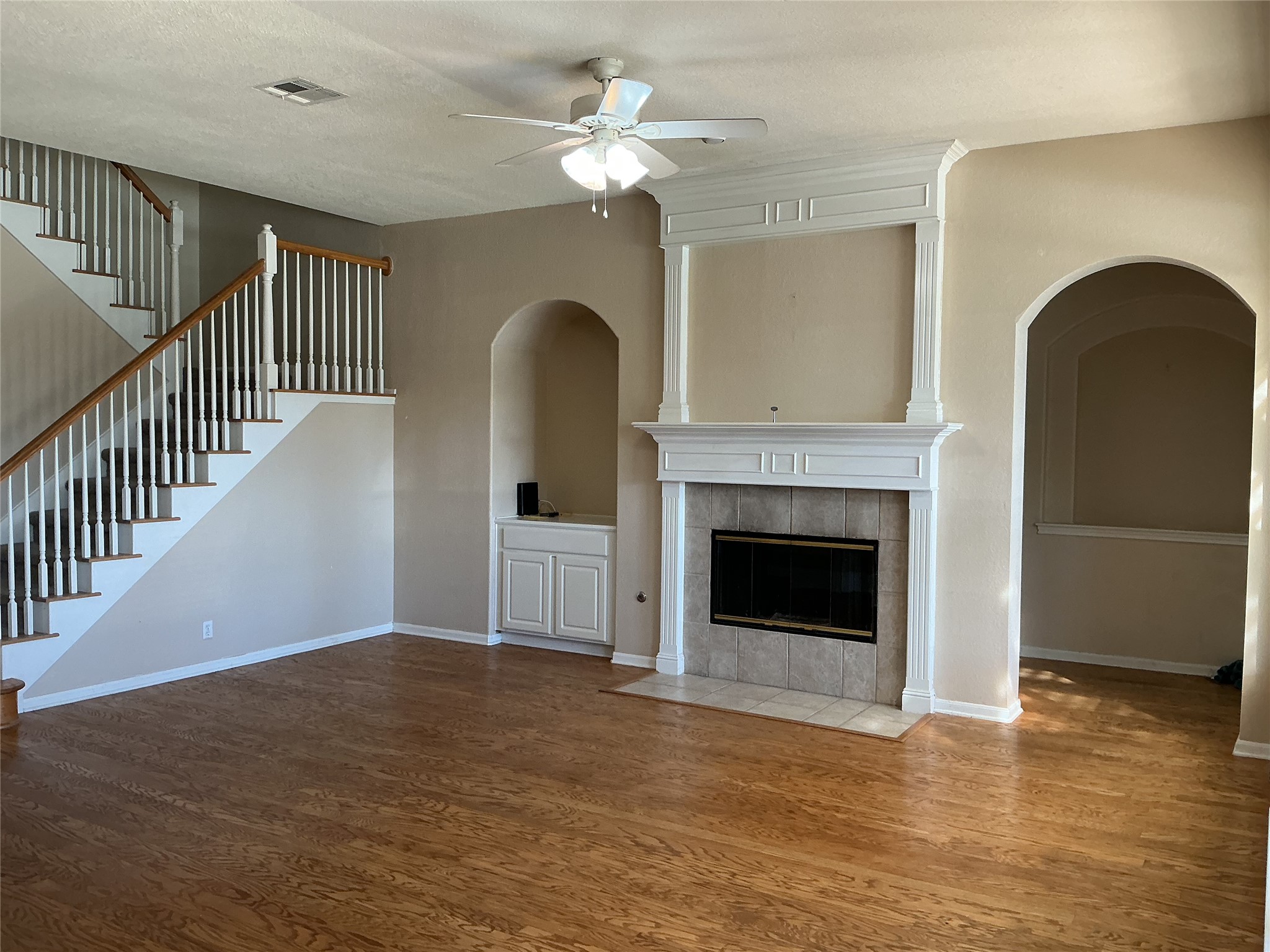 109 Fairfield Court Georgetown, TX 78633 - Photo 2 of 5 Unfurnished living room with ceiling fan, a tiled fireplace, wood finished floors, and arched walkways