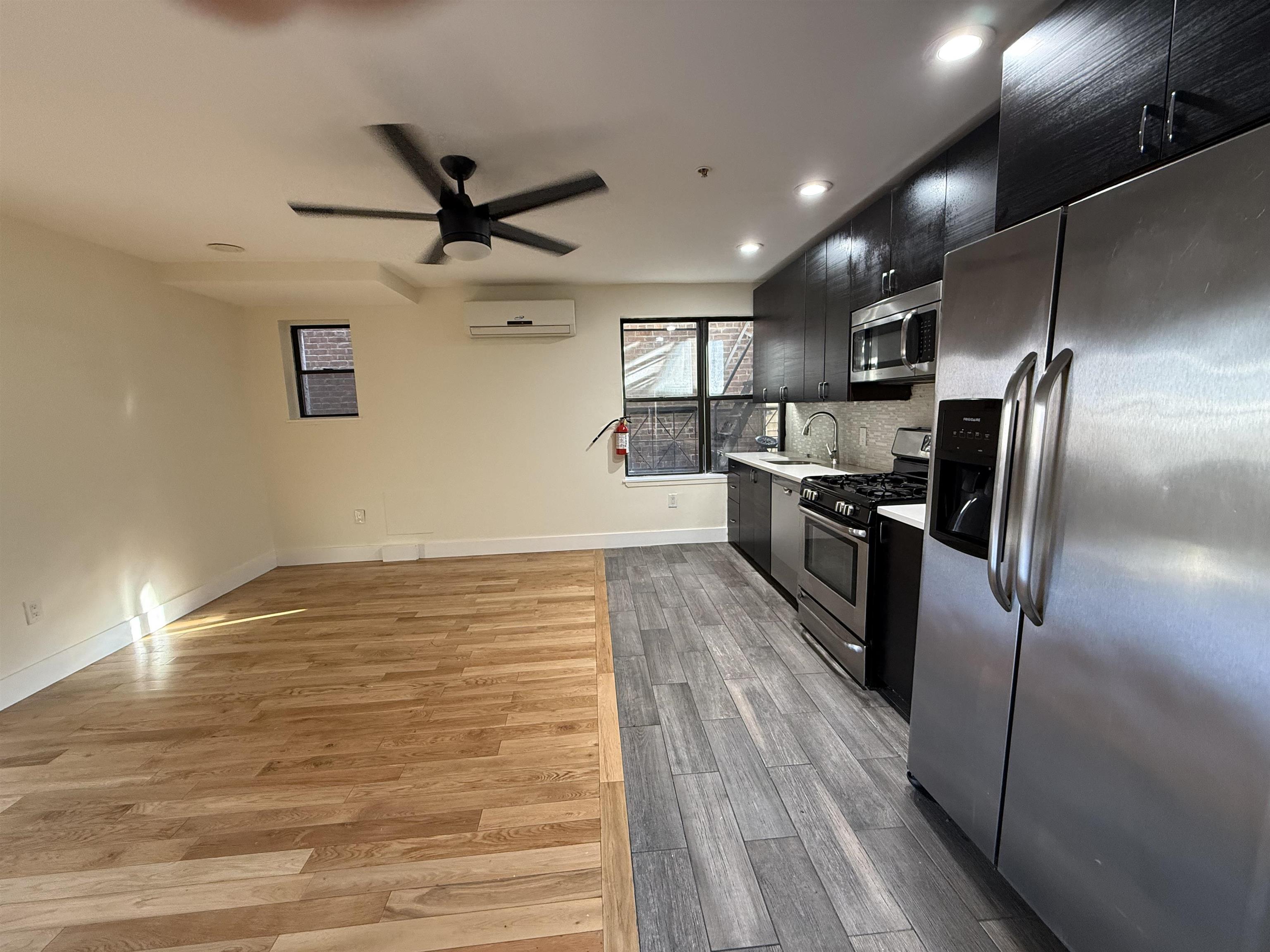 73-75 Ferry Street, Unit 7 Newark, NJ 07105 - Photo 2 of 11 an empty room with wooden floor kitchen view and a ceiling fan