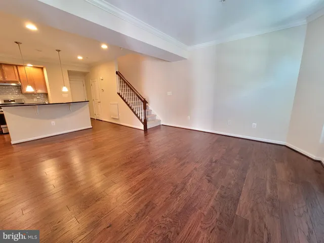 a view of an empty room with wooden floor and a kitchen