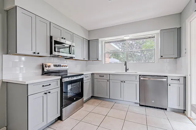 a kitchen with white cabinets appliances a sink and a window