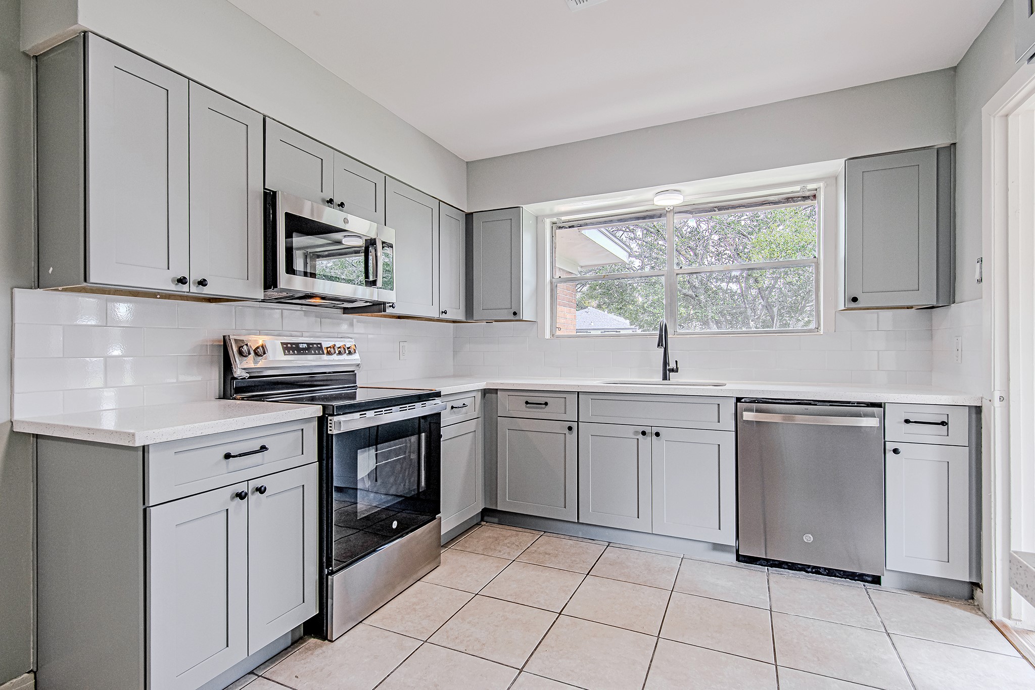 a kitchen with white cabinets appliances a sink and a window