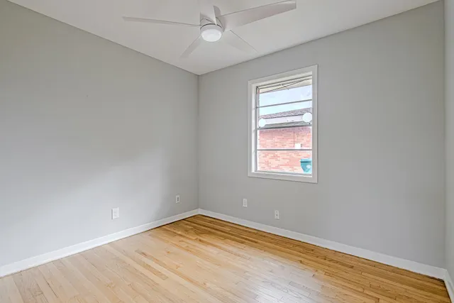 an empty room with wooden floor chandelier fan and windows