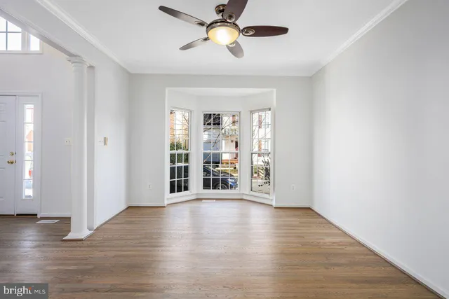 a view of an empty room with window and hardwood floor