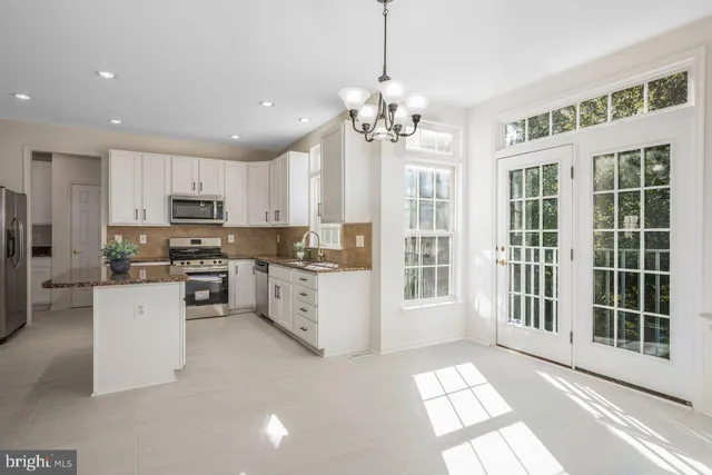 a large white kitchen with kitchen island a large window and stainless steel appliances