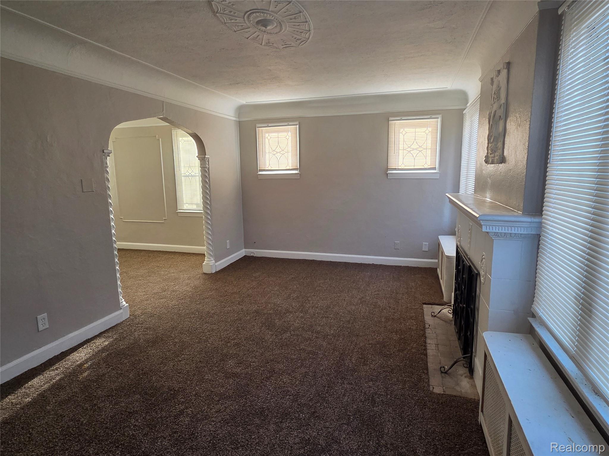 5274 Nottingham Road Detroit, MI 48224 - Photo 3 of 18 Unfurnished living room featuring arched walkways, dark carpet, and a fireplace with flush hearth